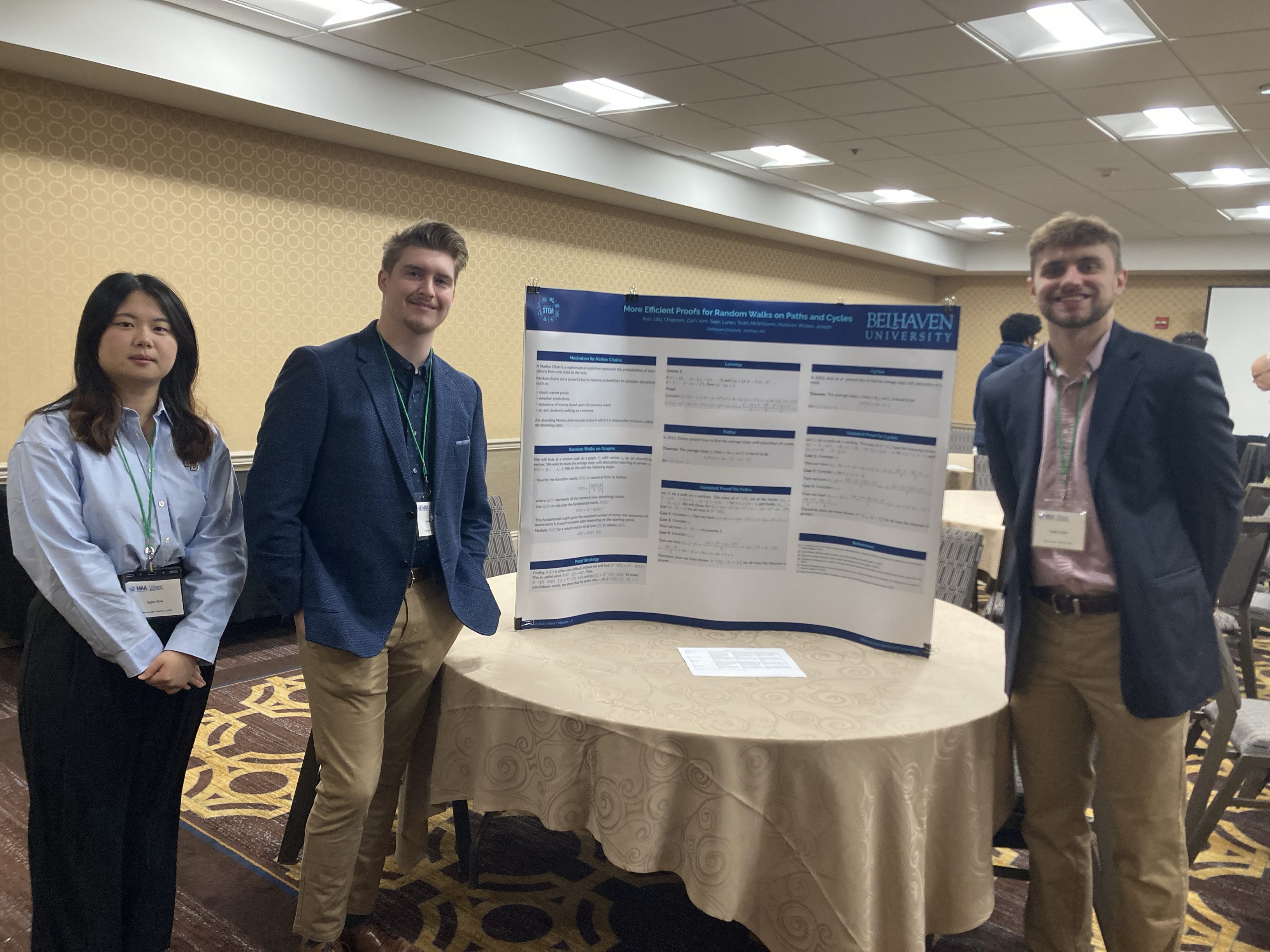 Two men and a woman standing around a trifold poster board in a conference meeting room.